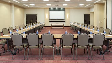 Una sala de conferencias con una mesa larga, sillas, botellas de agua y una pantalla para proyector.