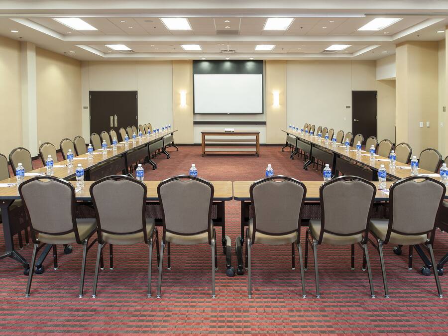 A conference room with a long table, chairs, water bottles, and a projector screen.