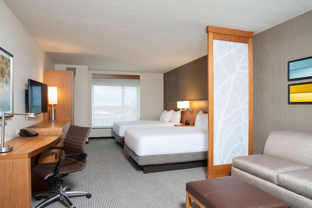 A hotel room with a desk, two beds, a sofa, and a TV.