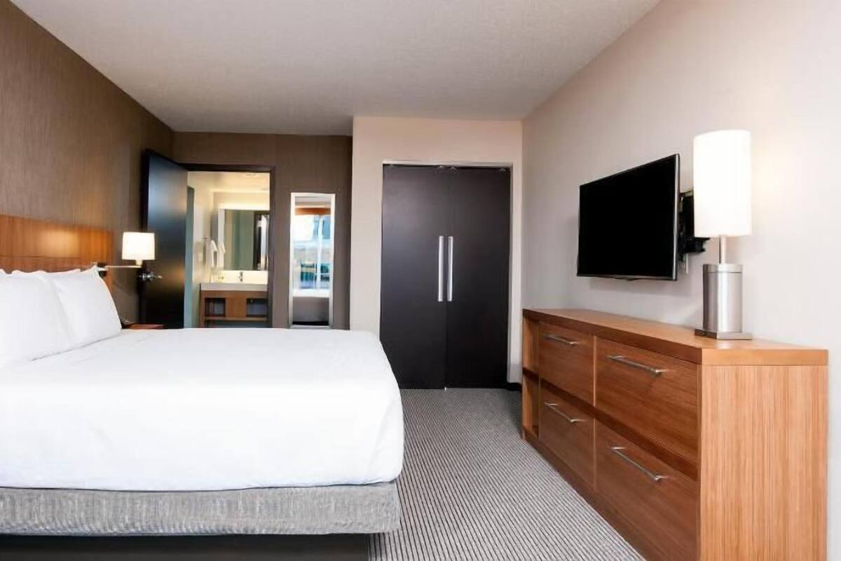 A hotel room with a large bed, a TV, a dresser, and a mirror.