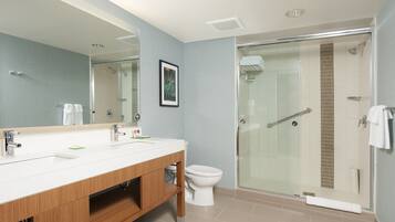 Een moderne badkamer met een houten wastafelmeubel, een witte wasbak, een toilet en een douchecabine met glazen wanden.