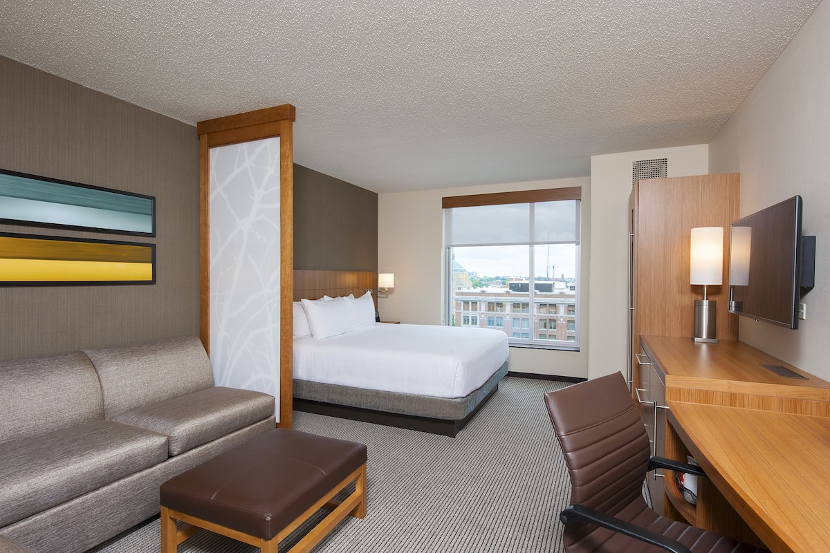 A hotel room with a bed, a sofa, a desk, and a TV.