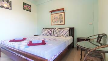 Een slaapkamer met een bed, kussens, een tafeltje en een stoel.