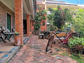 A courtyard with a brick pathway, wooden furniture, and a bicycle. - Baan Por Jai (Ko Lanta)