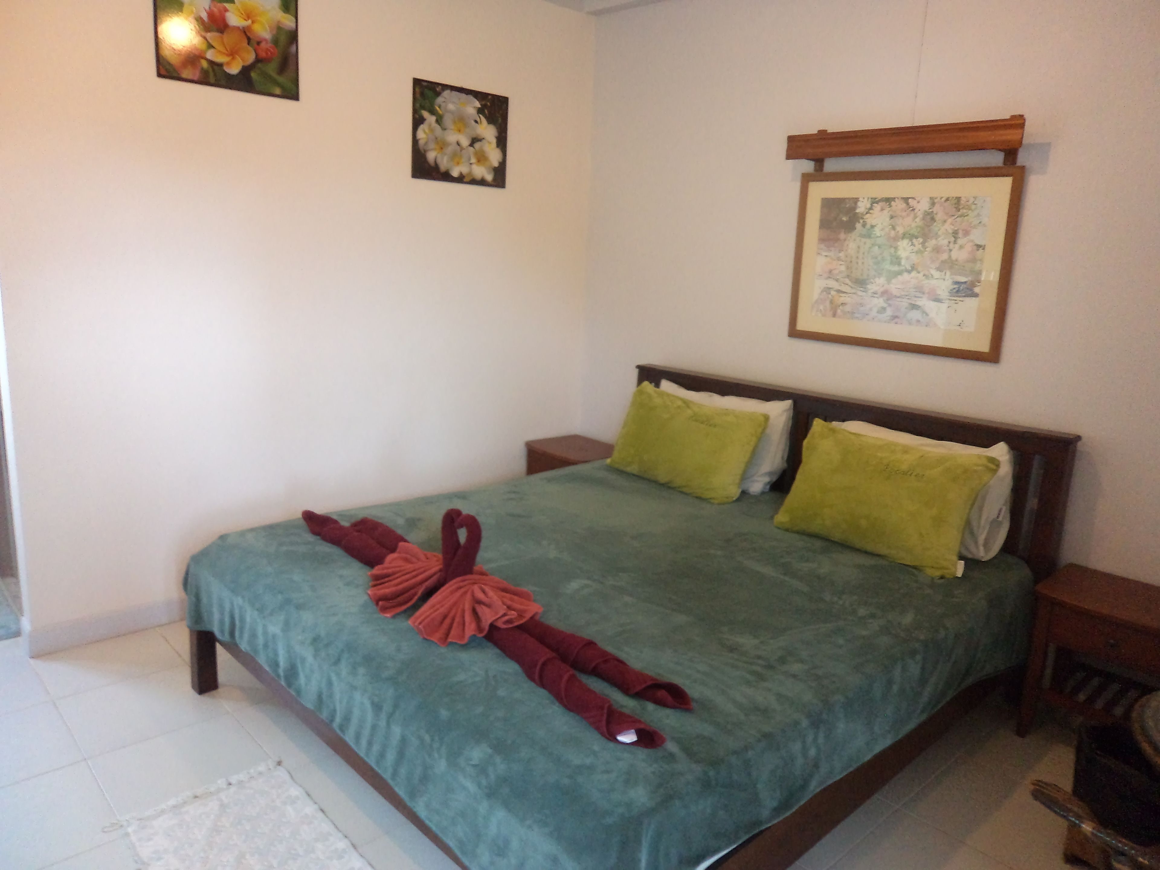 A neatly made bed with a green bedspread, two pillows, and two towels arranged in a decorative manner.
