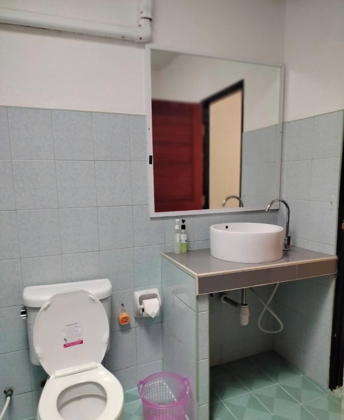 A bathroom with a toilet, sink, mirror, and a trash bin.