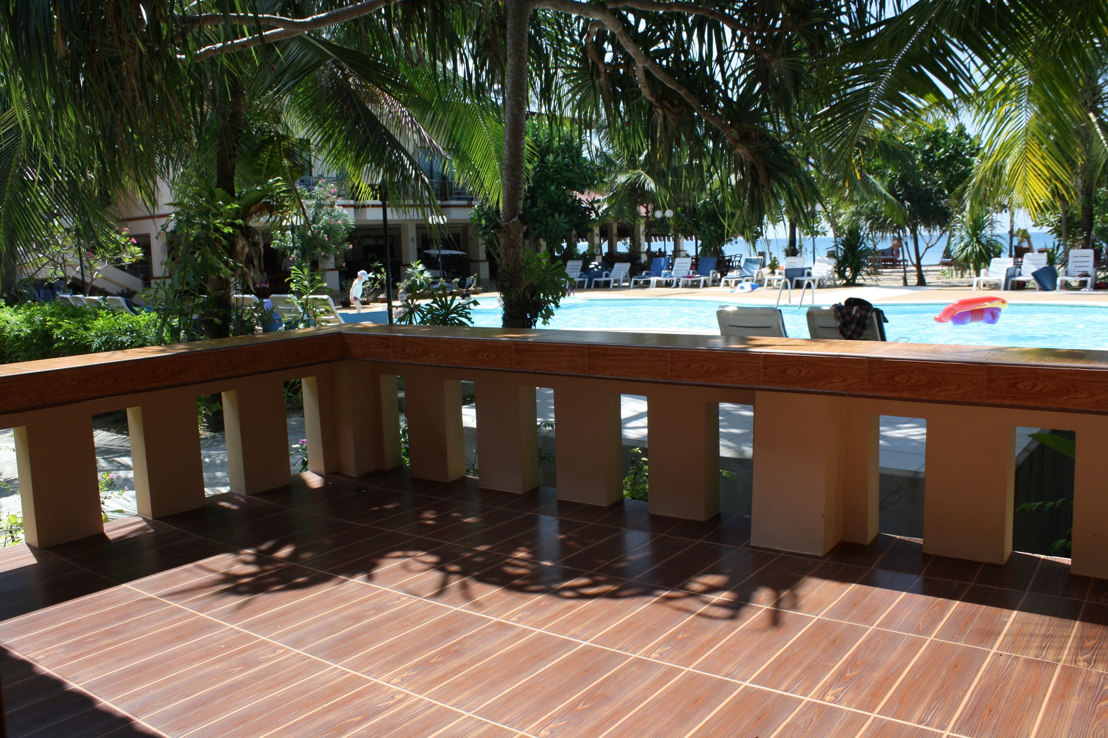 A pool area with a tiled deck, lounge chairs, and palm trees.