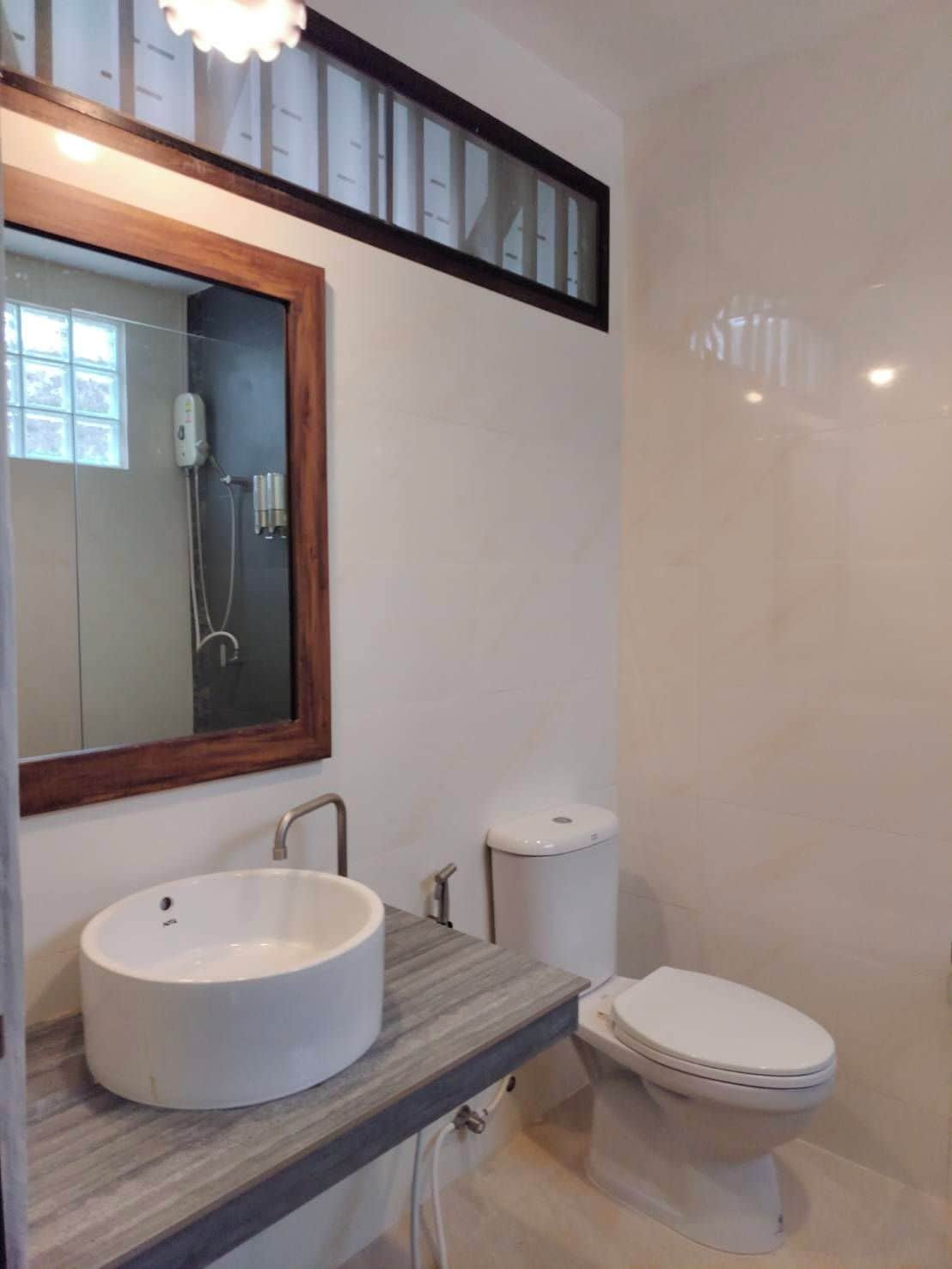 A bathroom with a large mirror, a vessel sink, a toilet, and a shower enclosure.