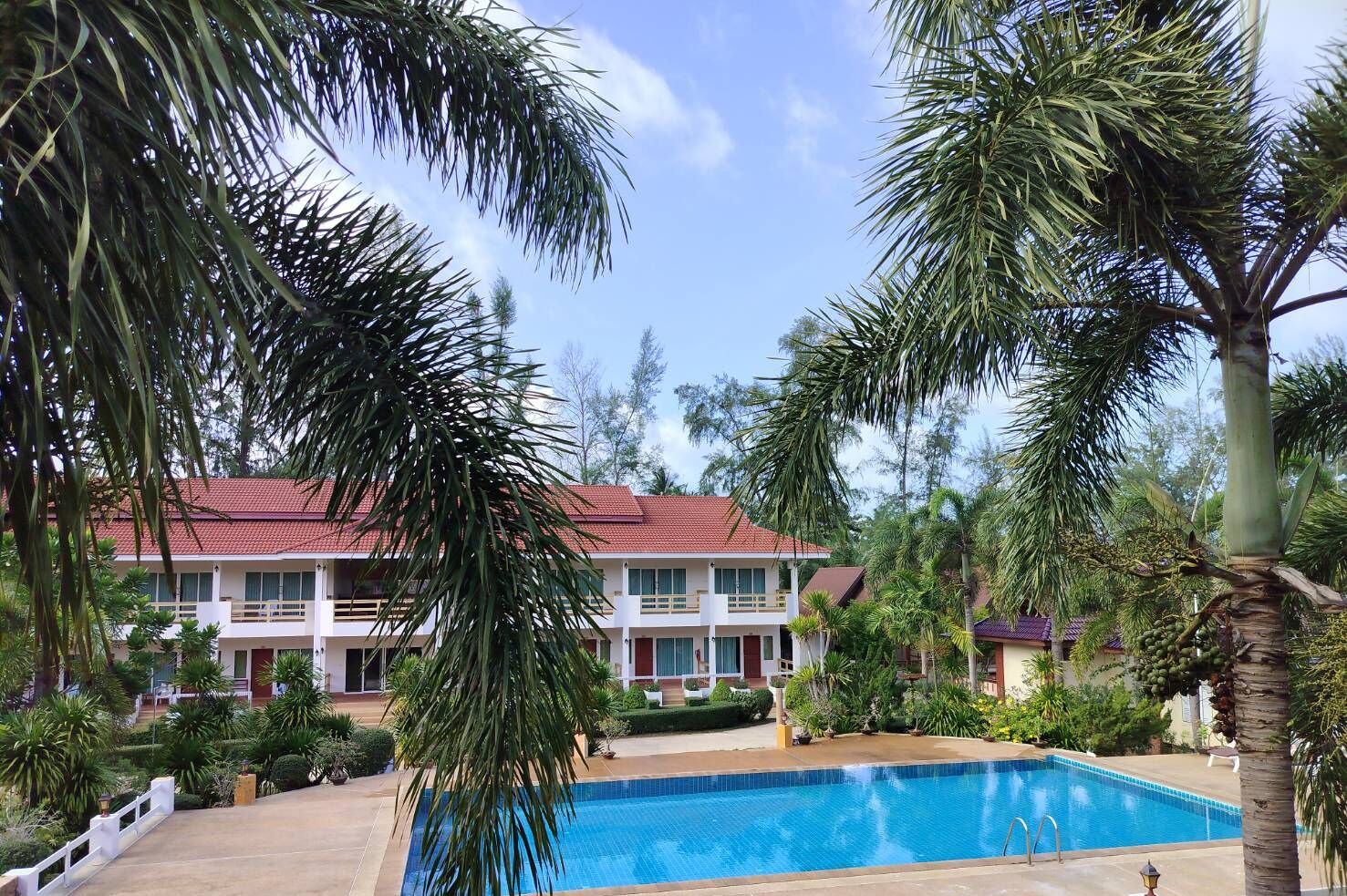 A two-story building with a red-tiled roof, surrounded by palm trees and a swimming pool.