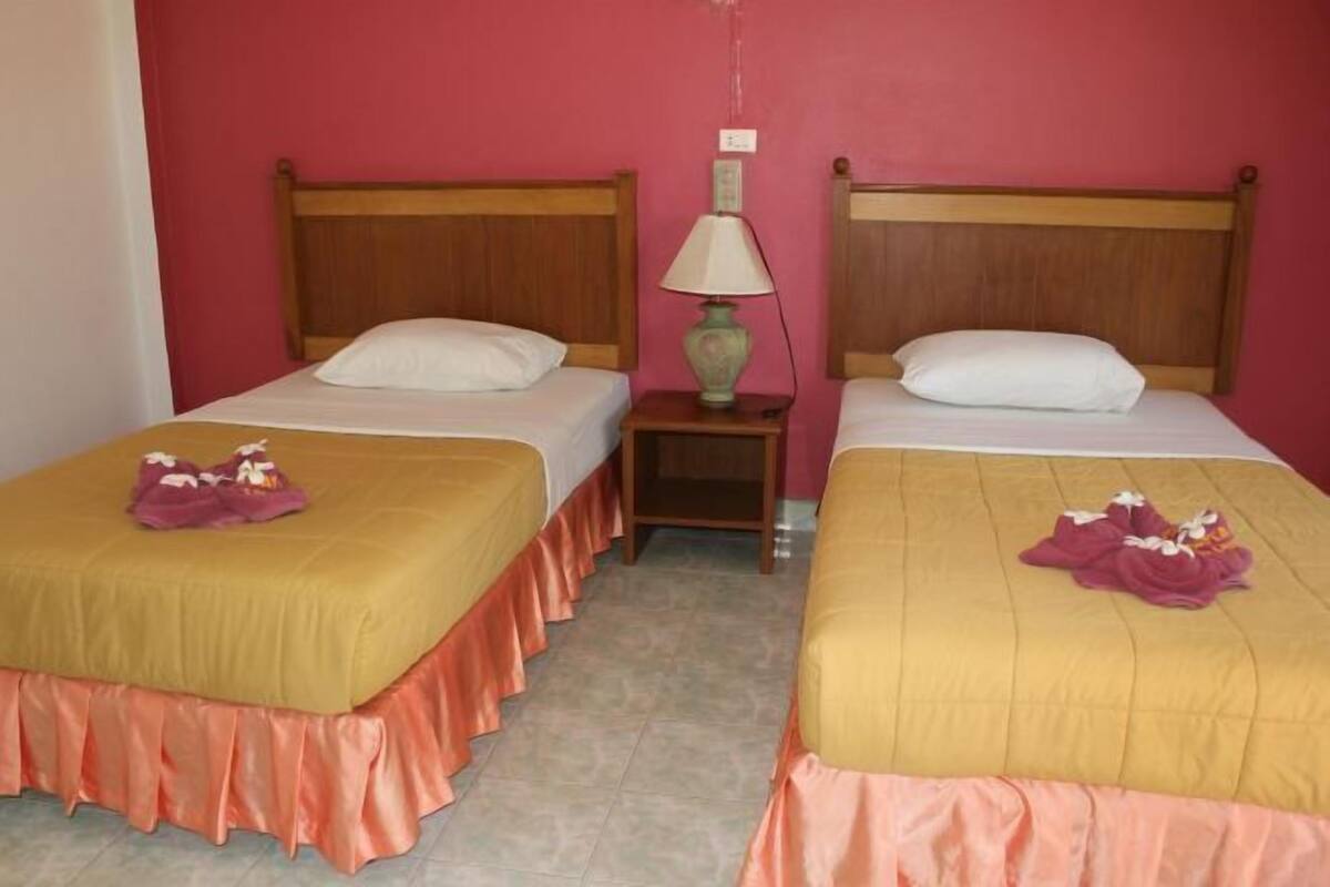 Two single beds with wooden headboards, a nightstand with a lamp, and a pink wall.
