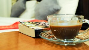 Une tasse de café en verre posée sur une soucoupe, avec un livre à côté.