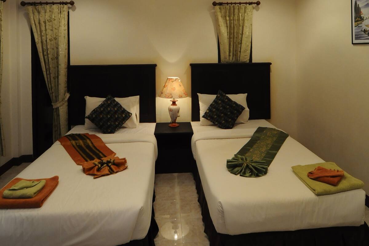 A hotel room with two beds, a nightstand with a lamp, and a ceiling light fixture.