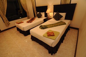 A hotel room with two beds, each with a pillow and a folded towel. There is a nightstand with a lamp between the beds. - N.T. Lanta Resort (Ko Lanta)