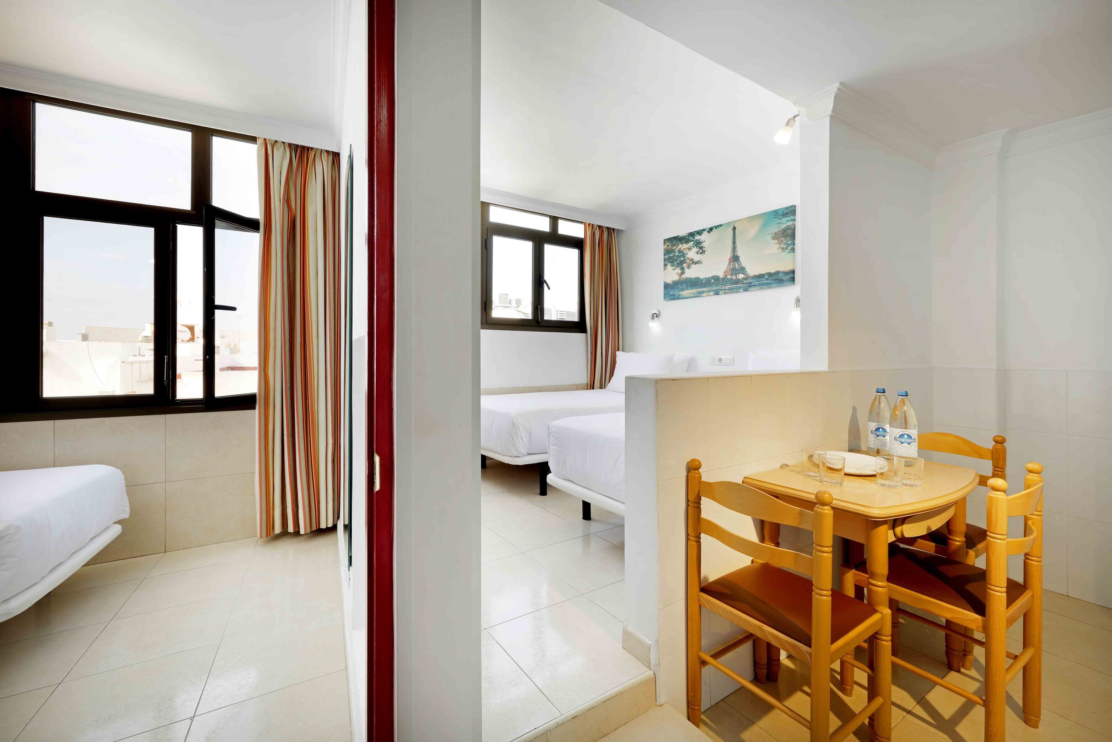 Una habitación de hotel con una cama, una mesa de comedor con sillas, una ventana con cortinas y un cuadro de la Torre Eiffel.