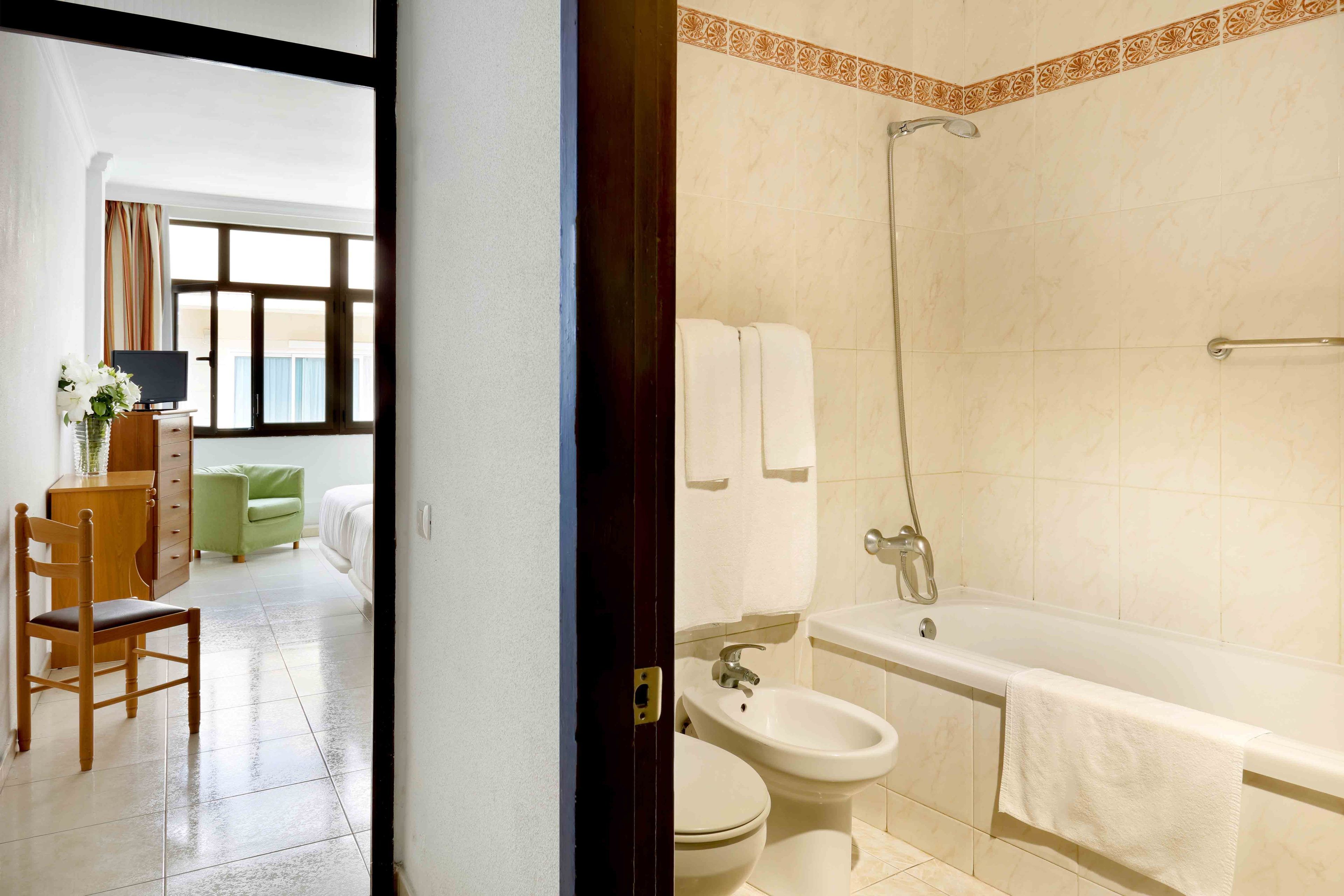 Habitación de hotel con una silla de madera, un sofá verde, un televisor y vistas al exterior a través de una ventana.