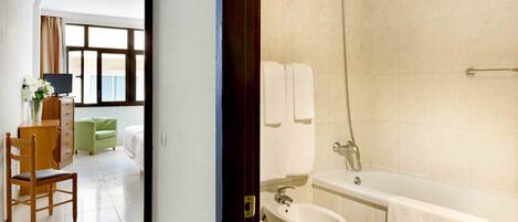 Habitación de hotel con una silla de madera, un sofá verde, un televisor y vistas al exterior a través de una ventana.