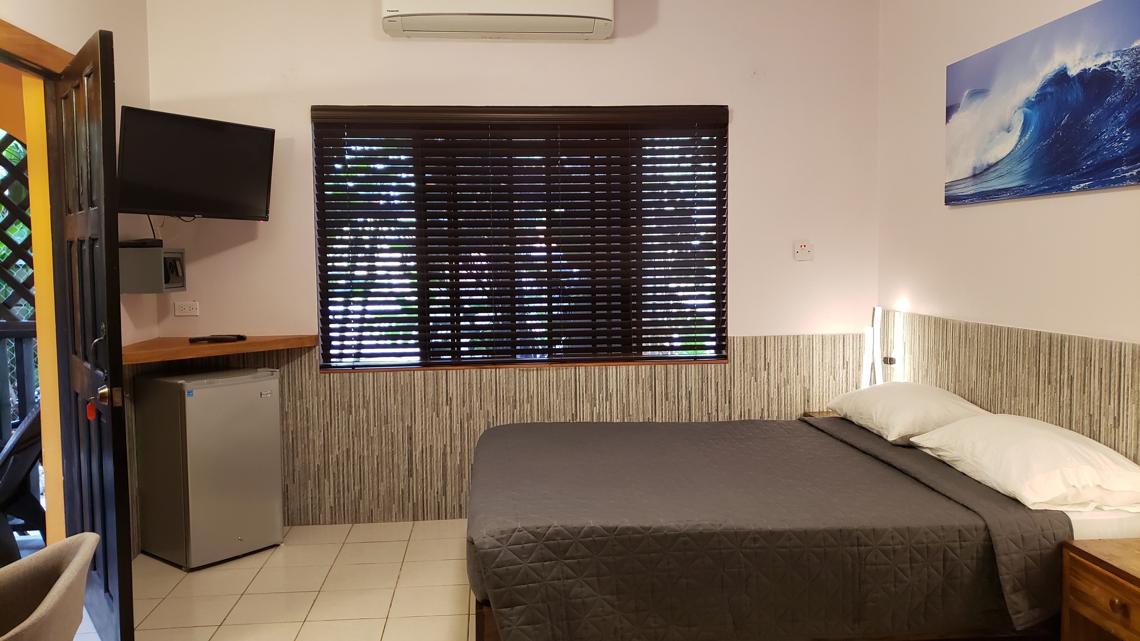 Une chambre avec un lit, une télévision, un petit réfrigérateur et une fenêtre avec des stores.