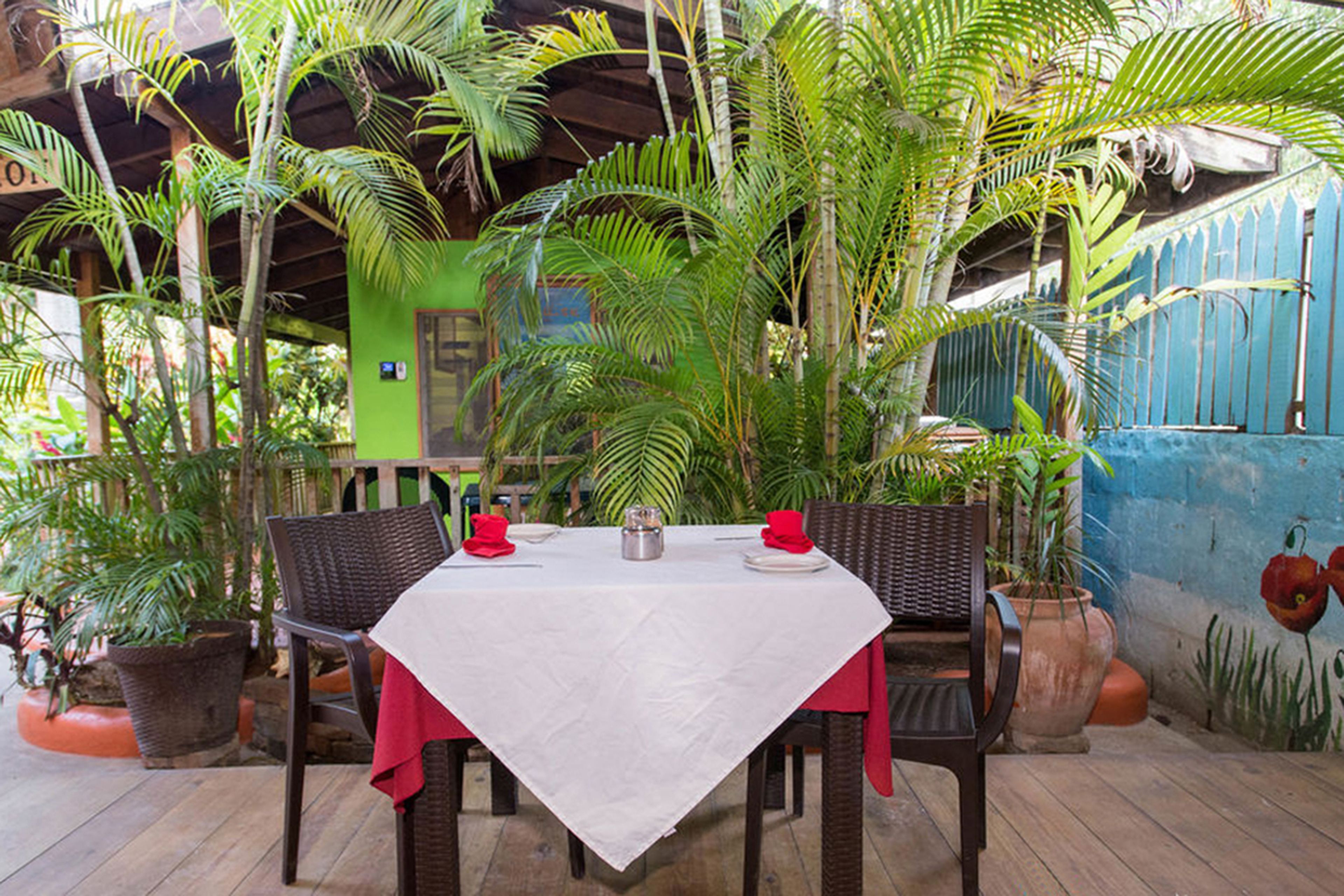 Ein Essbereich im Freien mit einem Tisch für zwei Personen, umgeben von Topfpflanzen und einer Holzterrasse.