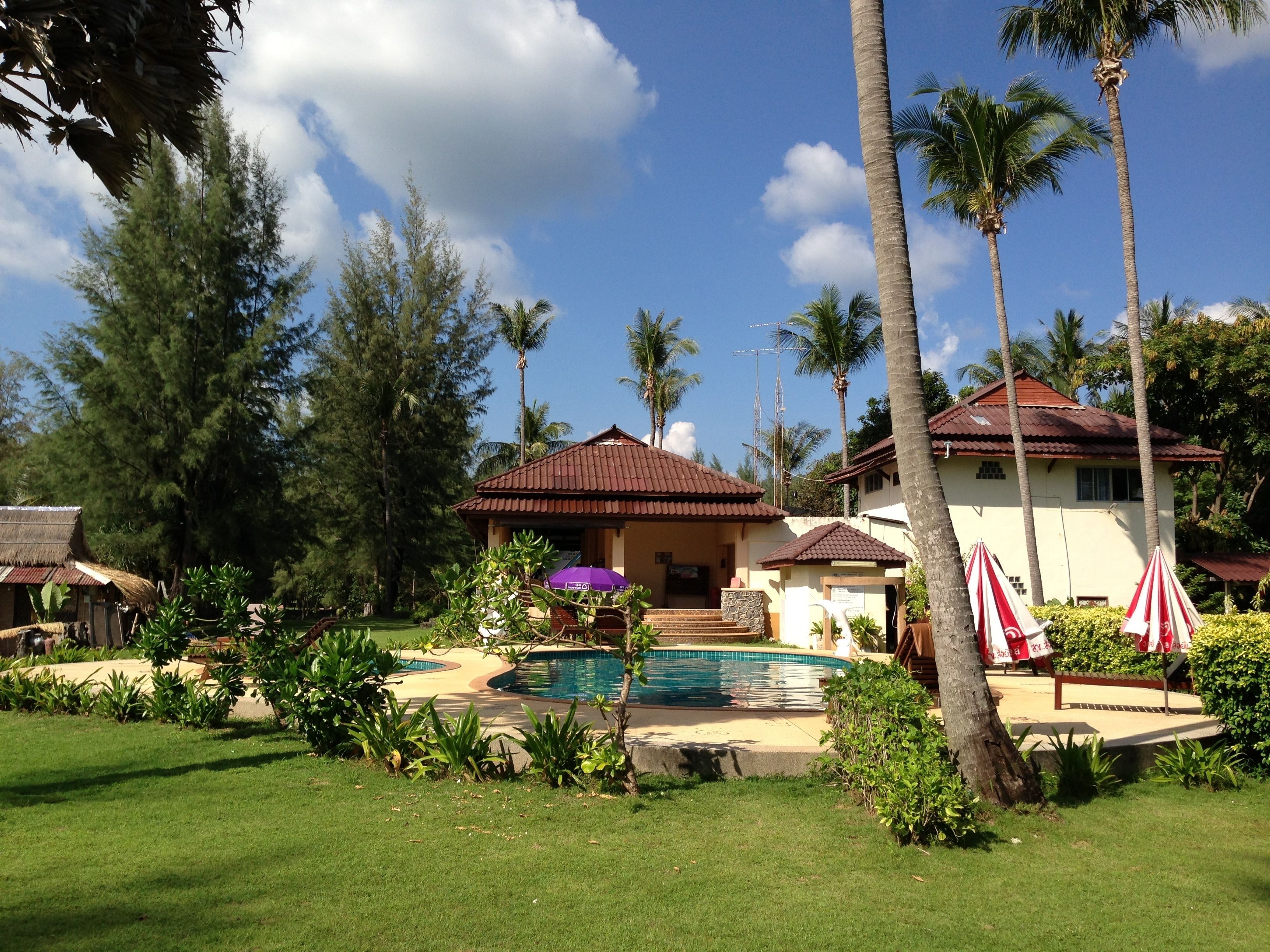 A resort with a swimming pool, palm trees, and a building with a red roof.