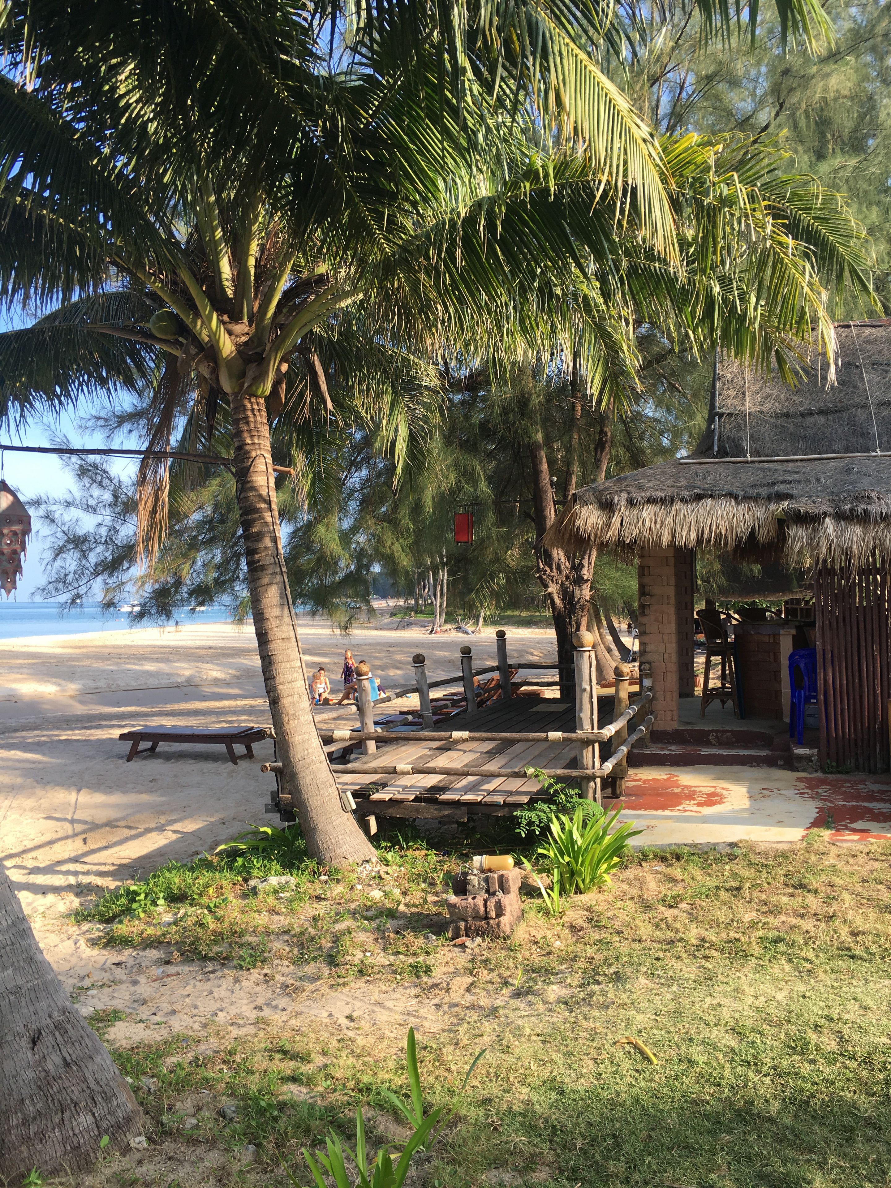 Une petite cabane au bord de la plage, avec un toit de chaume, une terrasse en bois et un banc.