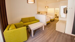 Una habitación de hotel moderna con un sofá verde, una cama blanca, una mesita y un escritorio.