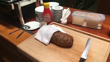 Una mesa con desayuno: pan, un cuchillo, una botella de kétchup y platos apilados.