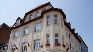 Un hotel de varios pisos con un estilo arquitectónico clásico, que destaca por una entrada imponente con escalones, ventanas amplias y jardineras en la fachada.