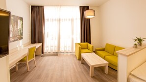 Una sala de estar moderna con piso de madera, un sofá amarillo, una mesa de centro blanca y un televisor sobre un mueble.