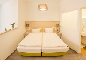 Cama doble con cabecera de madera, mesitas de noche y una planta pequeña en la pared.