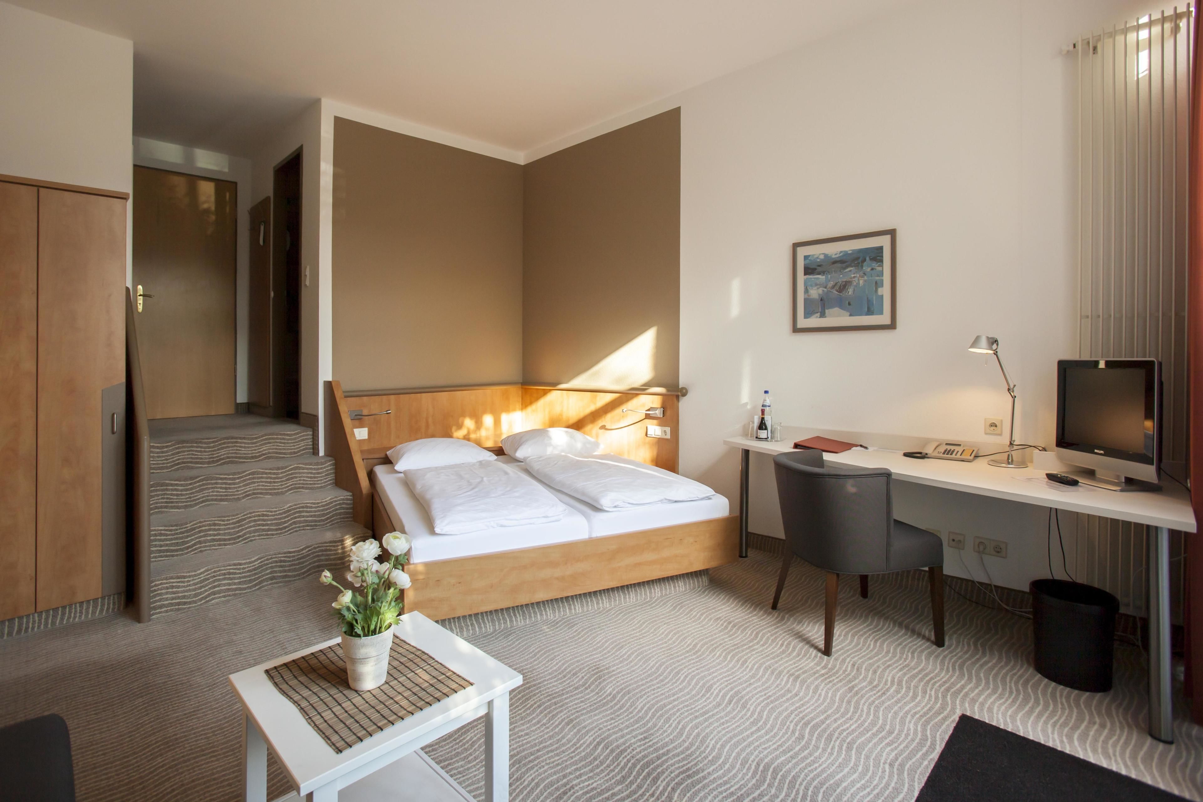 Une chambre d’hôtel avec un lit, un bureau, une chaise, une télévision et une petite table sur laquelle est posée une plante.