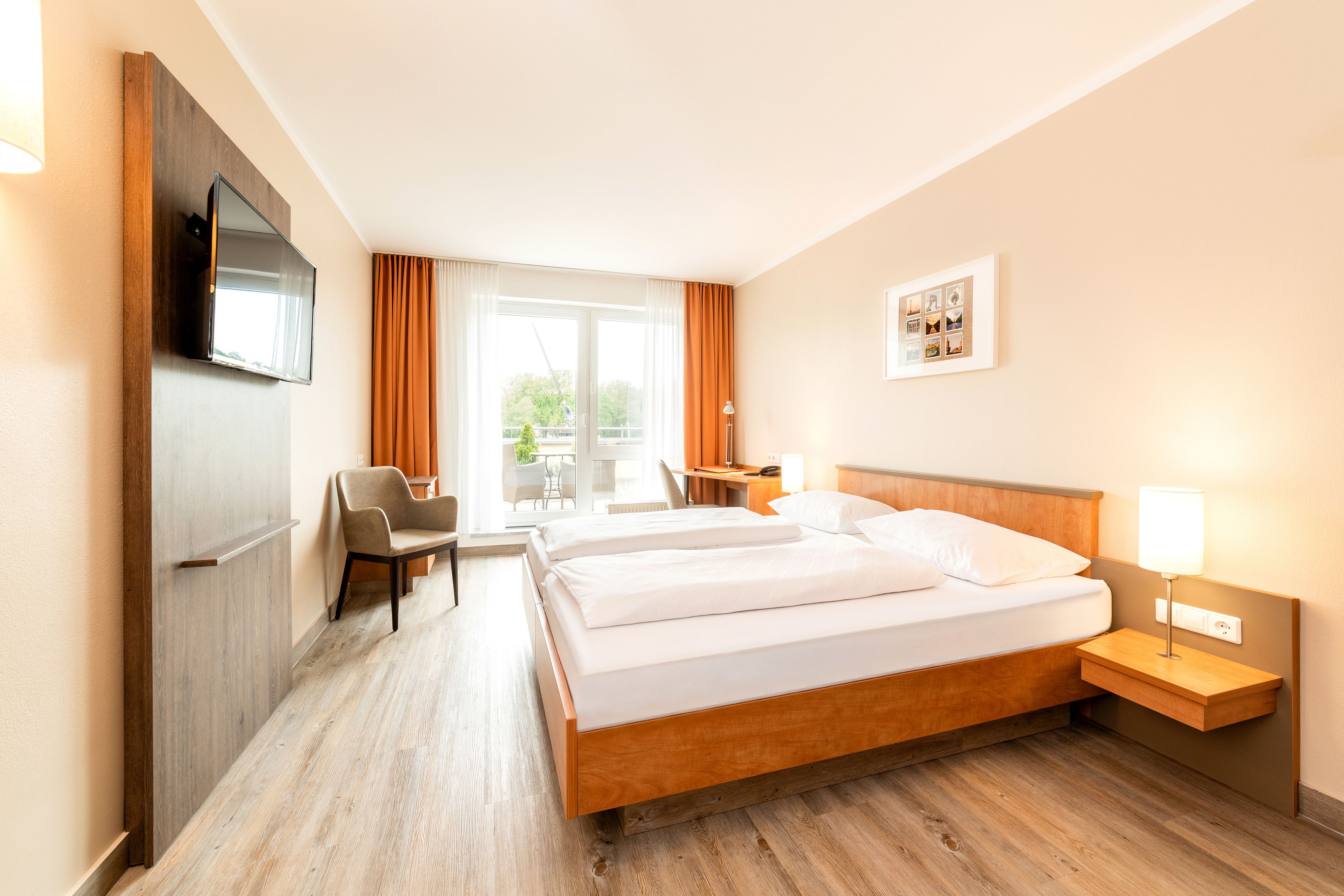 A hotel room with a wooden bed, a desk, a chair, a TV, and a window with curtains.
