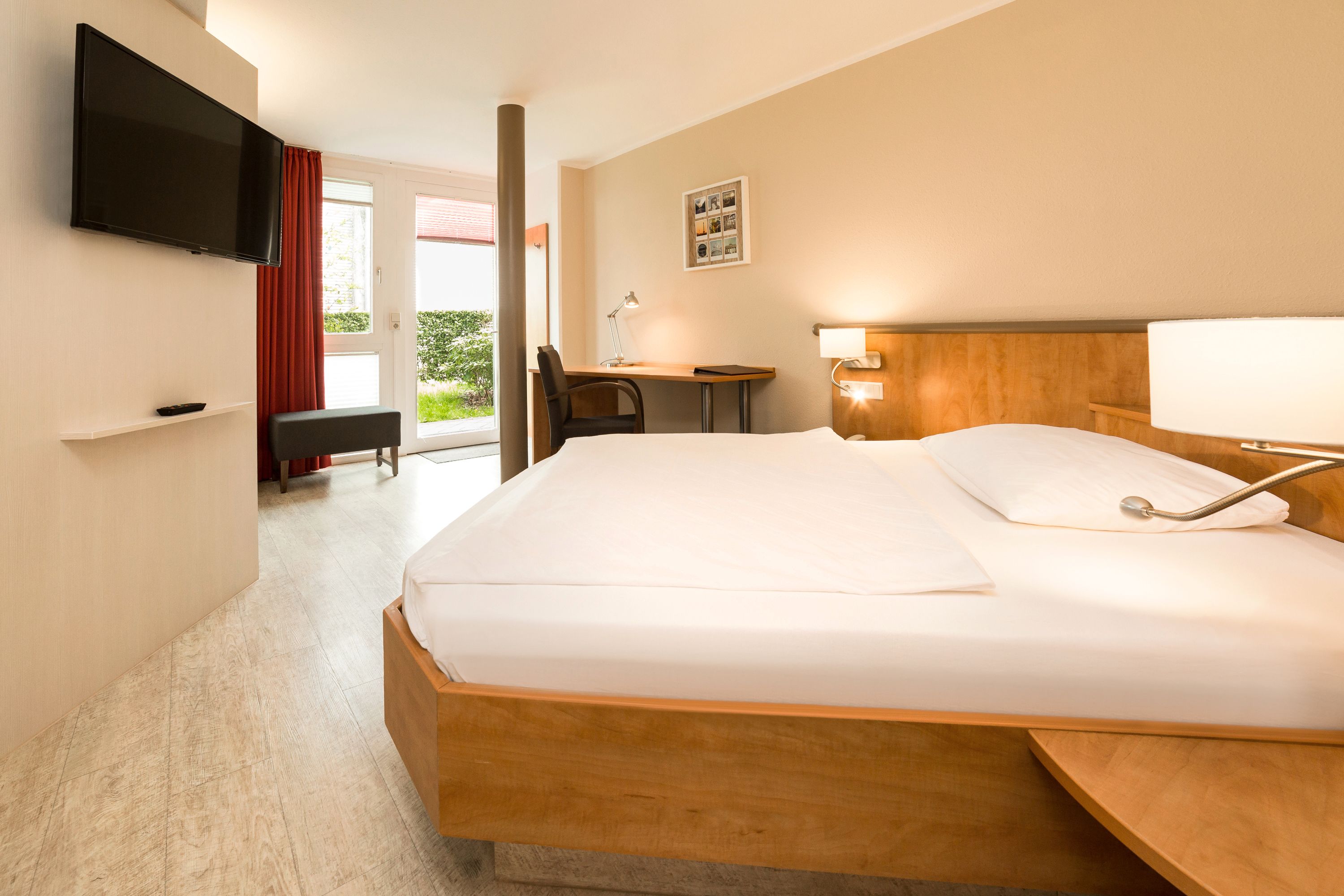 Una habitación de hotel con una cama grande, un escritorio, una silla, un televisor y una ventana con cortinas.