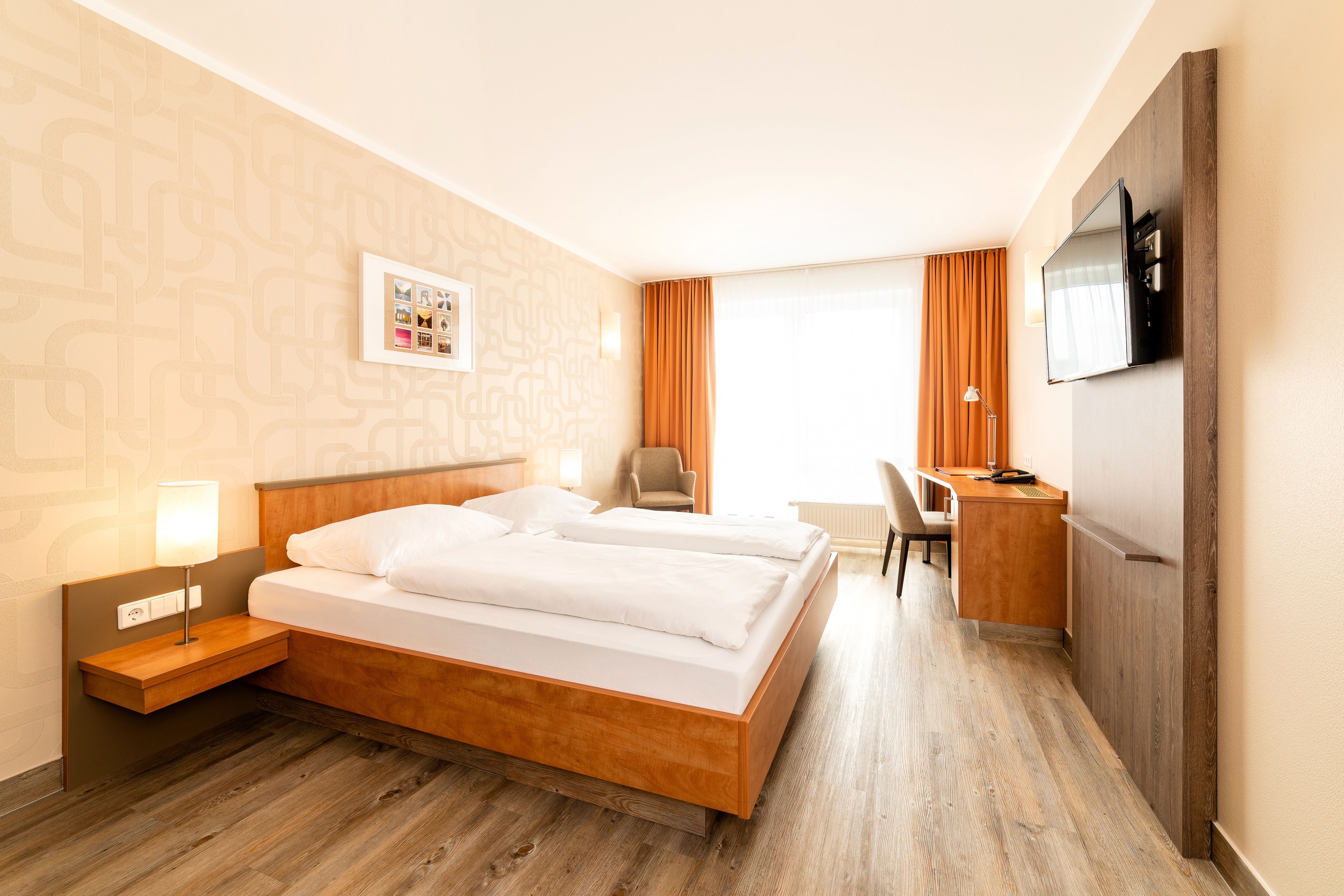 A hotel room with a wooden bed, a desk, a chair, and a TV mounted on the wall.