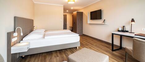 A modern hotel room with a bed, bedside table, lamp, TV, and a desk with a chair.