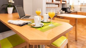 Un desayuno con una computadora portátil, dos vasos de jugo de naranja, un periódico y una taza blanca sobre una mesa de madera.