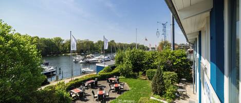 A riverside patio with tables and chairs, overlooking a marina with boats.