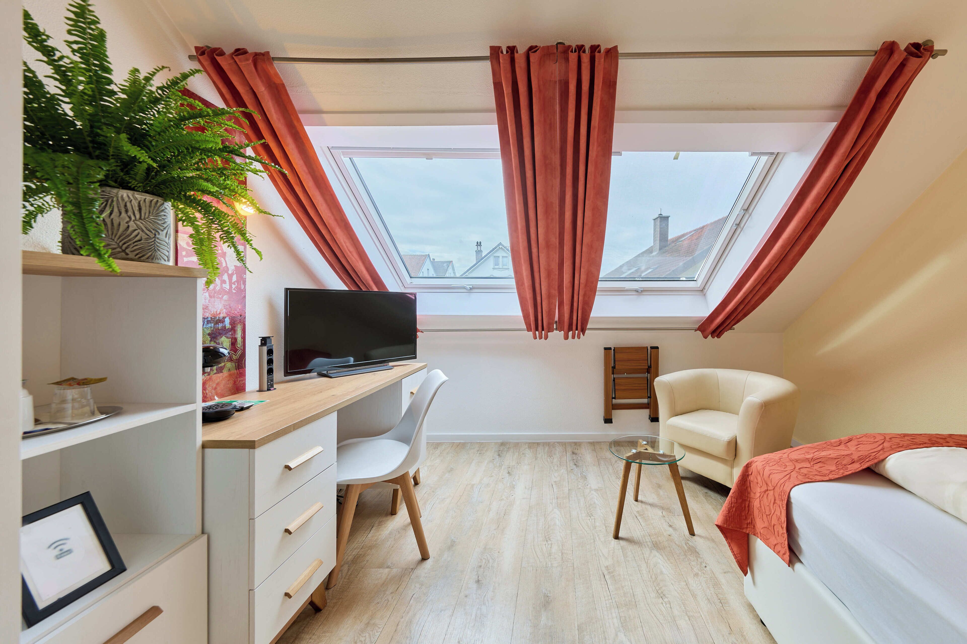 Een moderne slaapkamer met dakraam, bureau met computer, stoel, bed en een potplant.