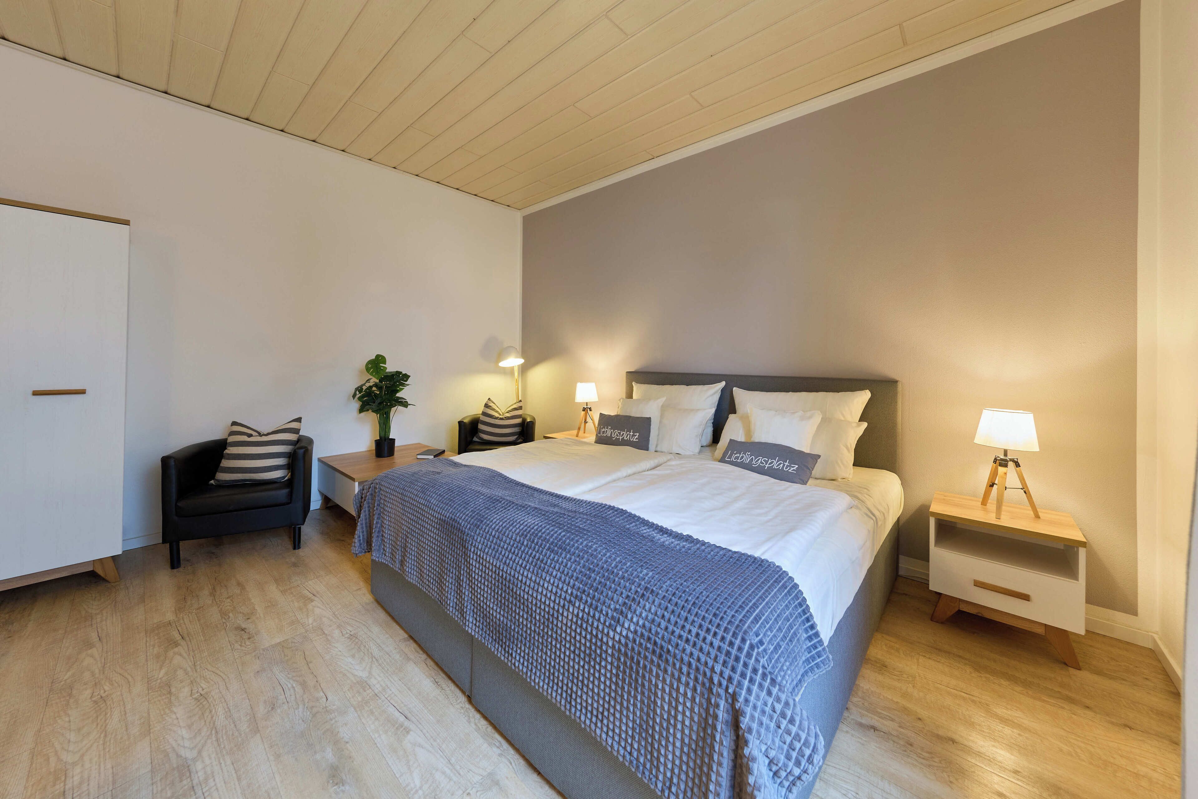 A modern bedroom with a large bed, bedside tables, a chair, and a lamp.