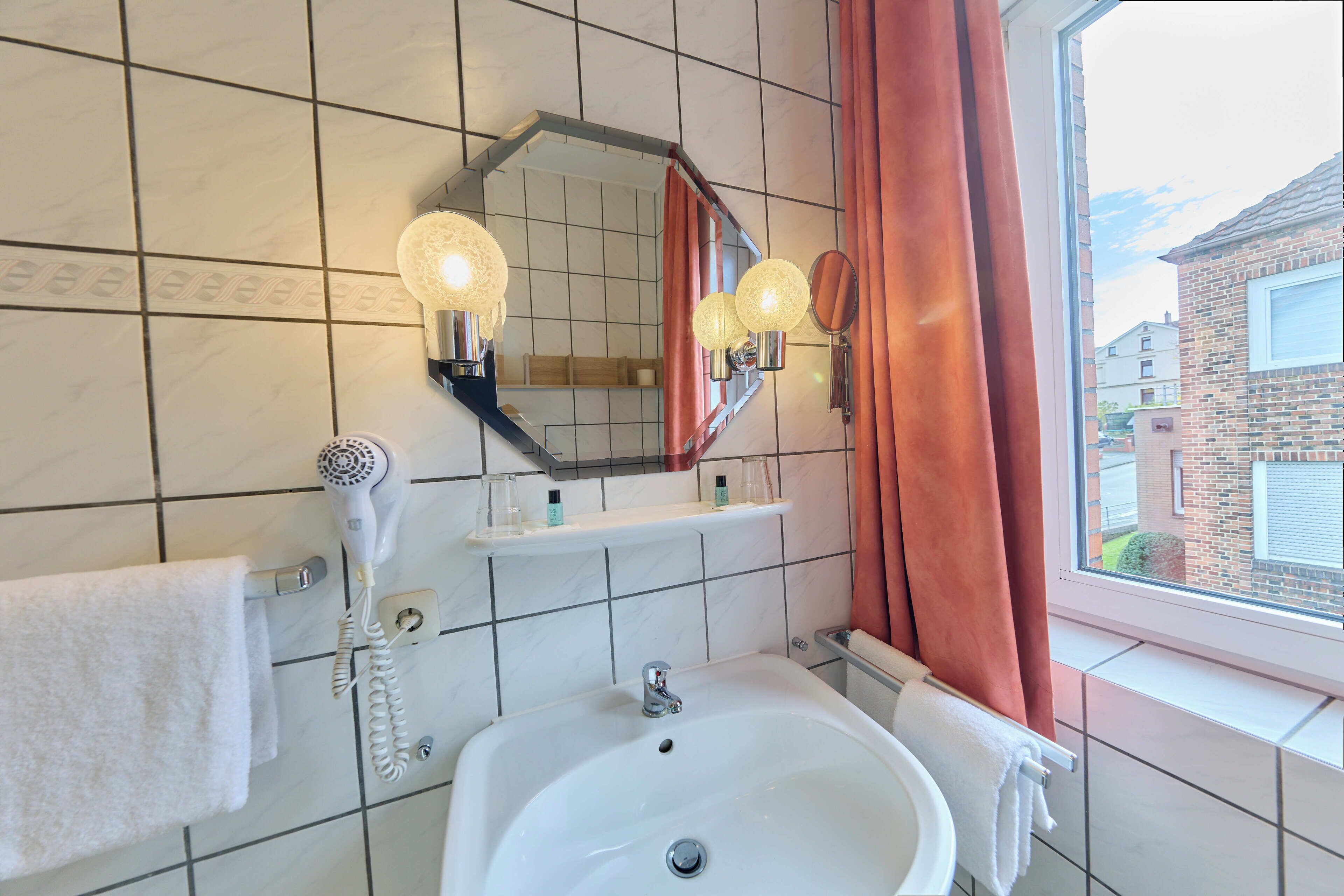 Ein Badezimmer mit Waschbecken, Spiegel, Fön und einem Fenster mit Vorhängen.