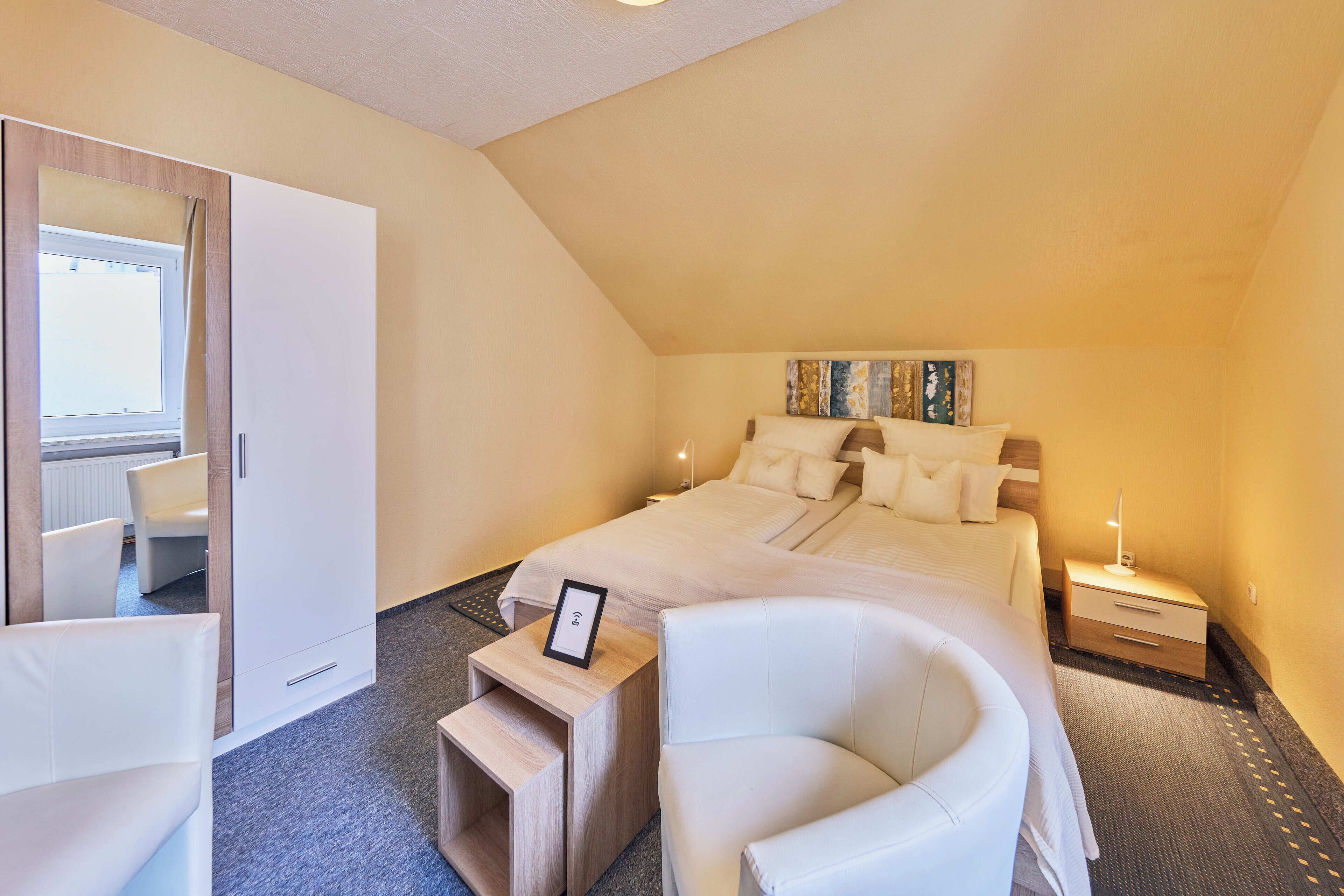 A bedroom with a bed, a chair, a bedside table, a nightstand, and a wardrobe.