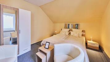 A bedroom with a bed, a chair, a bedside table, a nightstand, and a wardrobe.