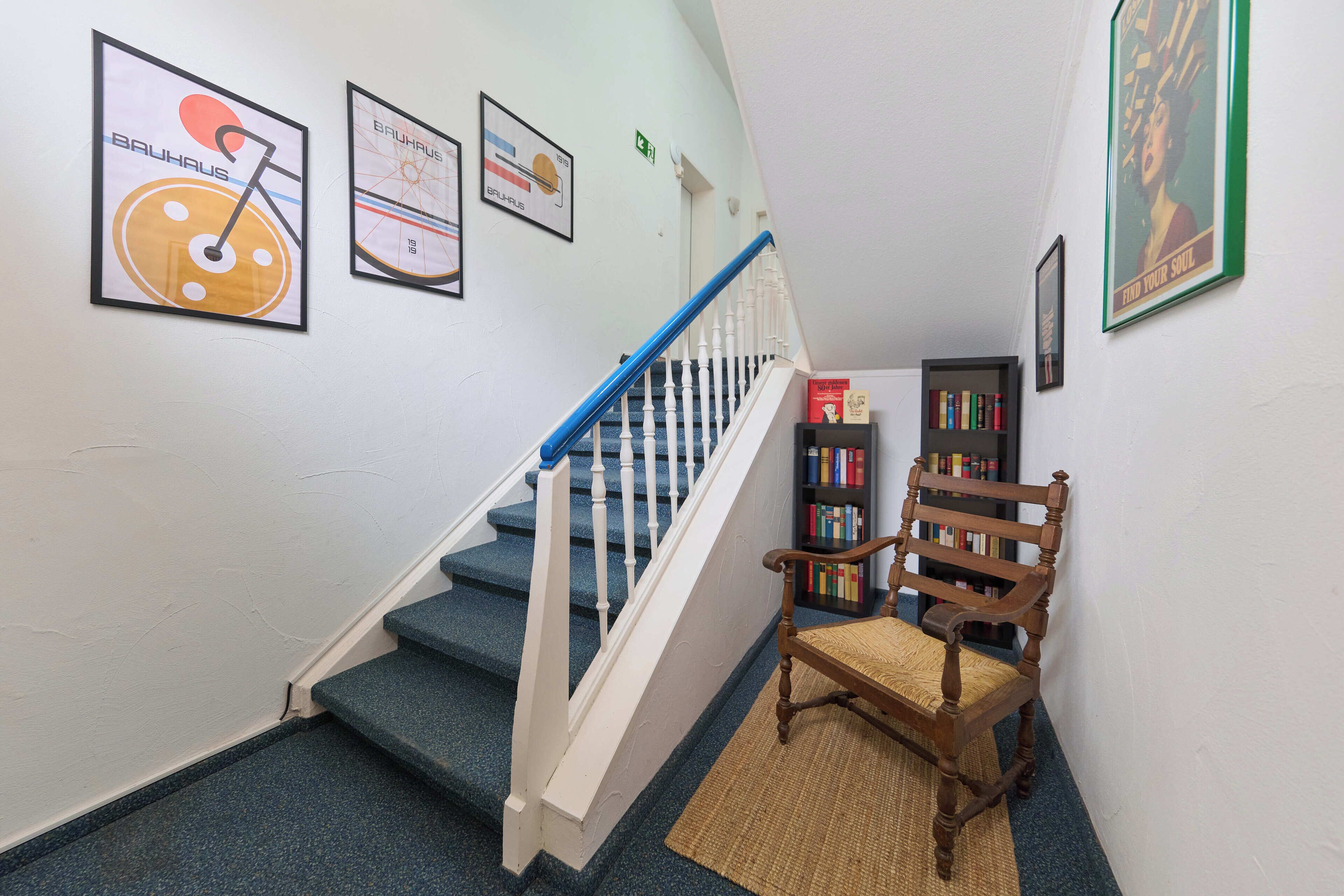 Una escalera con barandillas azules, una silla de madera y carteles enmarcados en la pared.