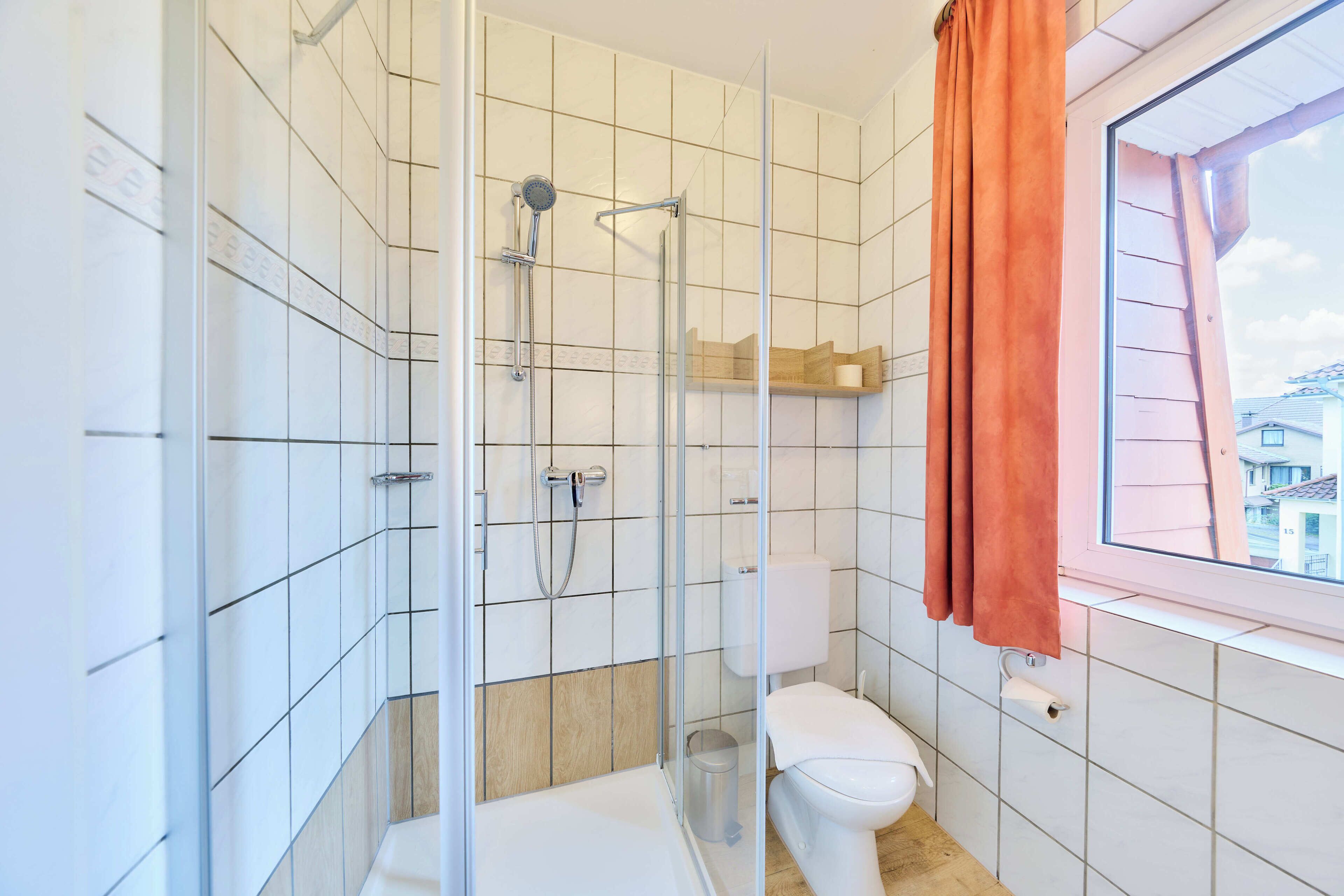 A bathroom with a glass-enclosed shower, a toilet, and a window with a view of buildings.