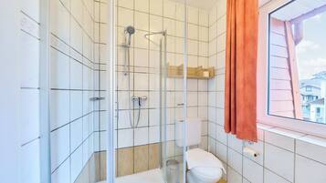 A bathroom with a glass-enclosed shower, a toilet, and a window with a view of buildings.
