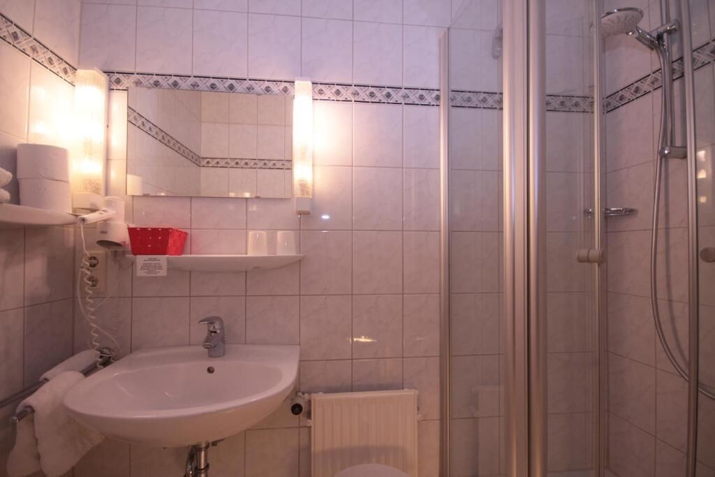 A bathroom with a sink, mirror, shower, and tiled walls.
