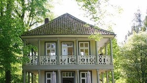 Een gebouw met twee verdiepingen en een balkon, omringd door een tuin met gele bloemen.