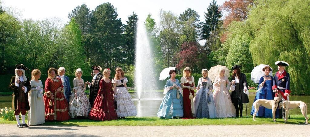 Un grupo de personas vestidas con trajes de época posando en un parque con una fuente.