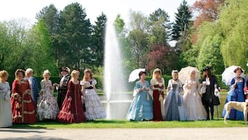 Un grupo de personas vestidas con trajes de época posando en un parque con una fuente.