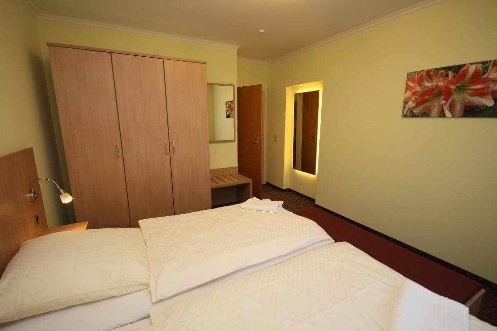 Une chambre d’hôtel avec un lit, une armoire, un miroir et un tableau au mur.