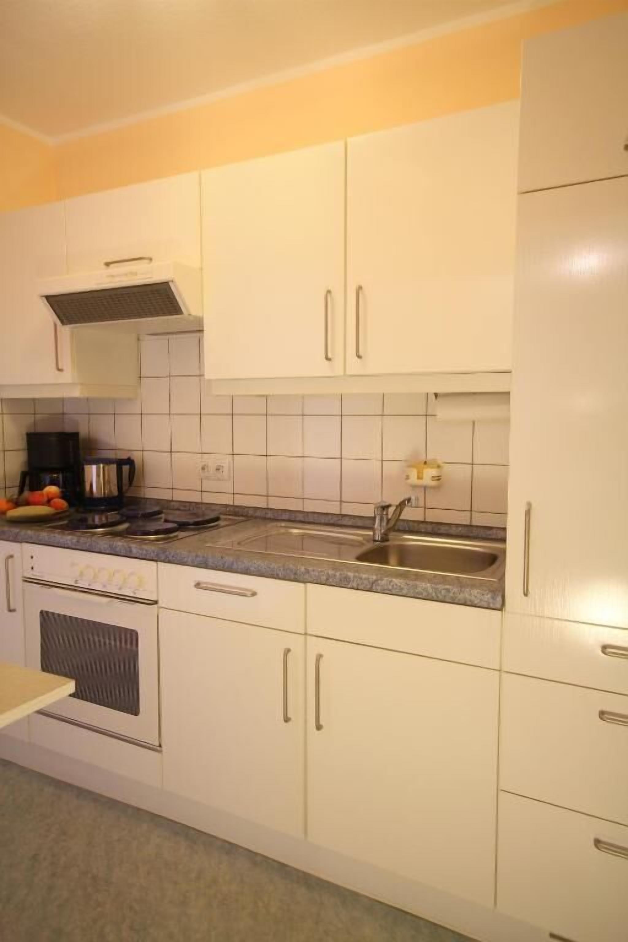 A kitchen with white cabinets, a stainless steel sink, a coffee maker, and a microwave.